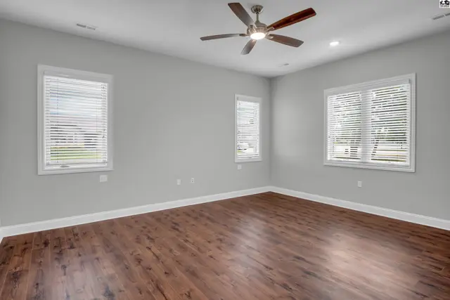 Spacious room with wood-look flooring, neutral walls, and a ceiling fan.