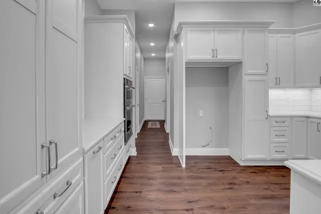 This spacious kitchen features white cabinetry, built-in ovens, and dark wood flooring.