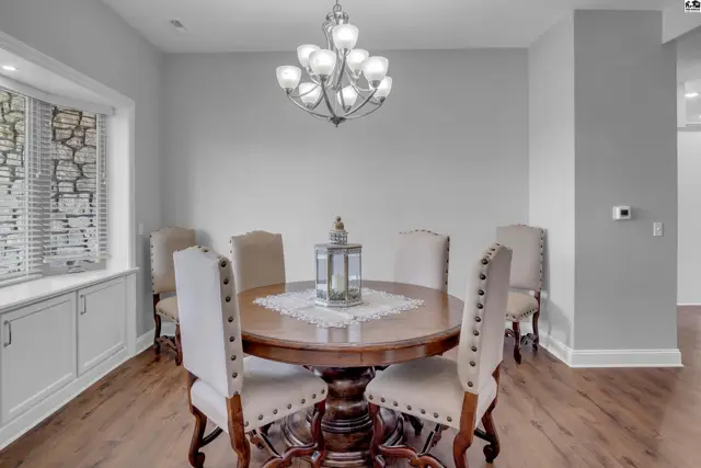 A round wooden dining table with six chairs is centered in a room with wood floors.