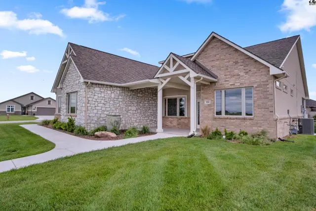 This home features a stone and brick exterior with a covered entryway and manicured lawn.
