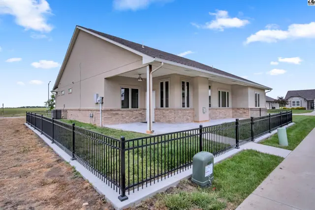 Covered patio with stone accents and a black metal fence surrounds this stucco home.