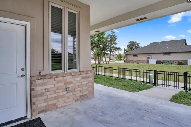 Covered porch with concrete floor, brick accent, and a white door leads to a grassy yard.