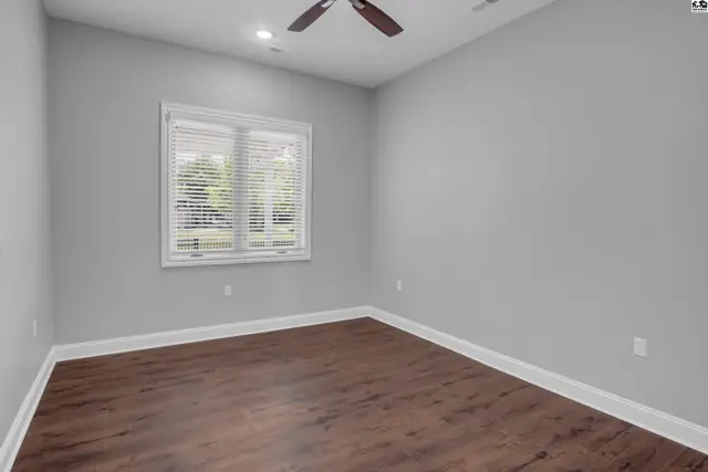 This room features a ceiling fan, wood-look flooring, and a large window with blinds.