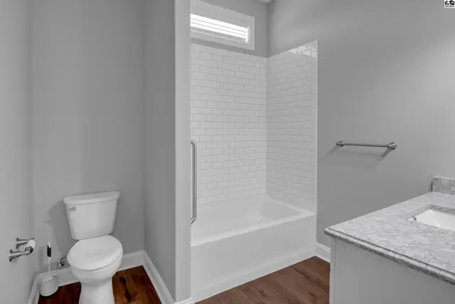 This bathroom features a white toilet, a bathtub with white subway tile surround, and a granite-topped vanity.