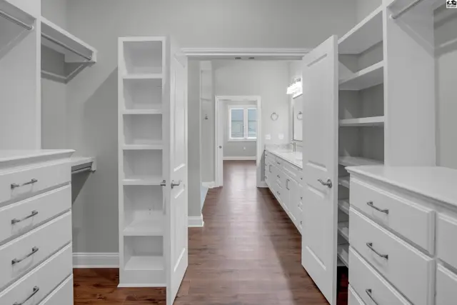 Spacious walk-in closet with built-in shelving and drawers opens to a bathroom.