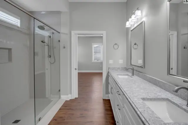 Spacious bathroom features a glass-enclosed shower and double vanity with granite countertops.