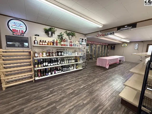 Interior view of a retail space with wood-look flooring, shelves stocked with beverages, and a display table.