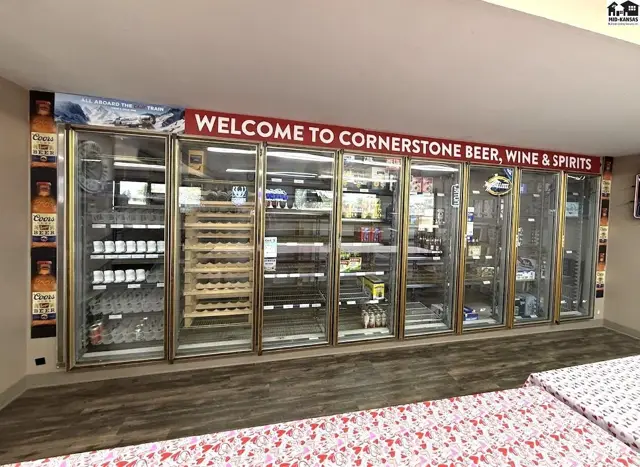 Glass-fronted refrigerators display beer, wine, and spirits in a well-lit store with a "Welcome" sign.