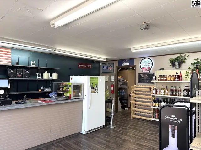 Interior view of a retail space with a counter, refrigerator, shelves stocked with bottles, and wood-look flooring.