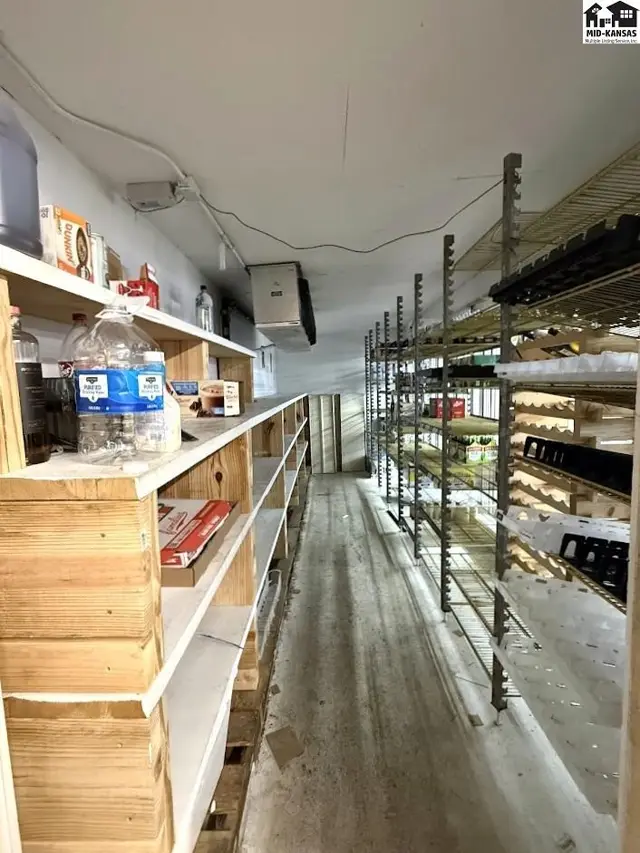 Commercial walk-in cooler with extensive shelving, concrete floor, and industrial cooling unit.