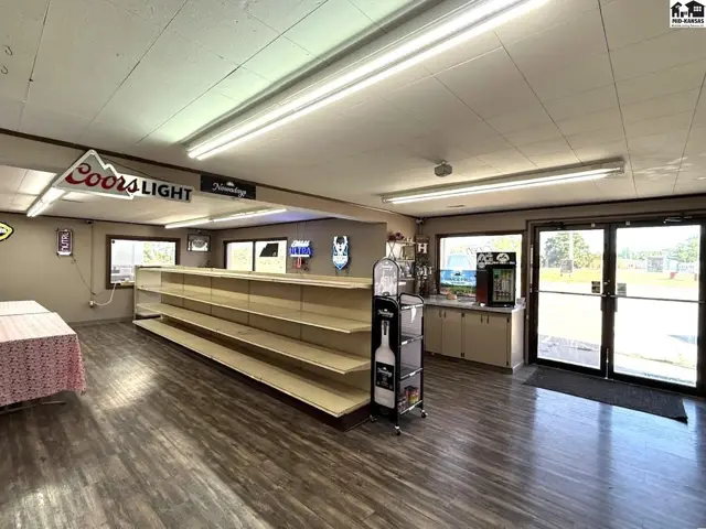Interior view of a commercial space with long shelving, a beverage cooler, and double glass doors.