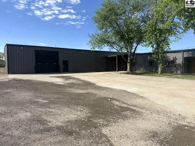 Dark metal industrial building with a large roll-up door and gravel lot.