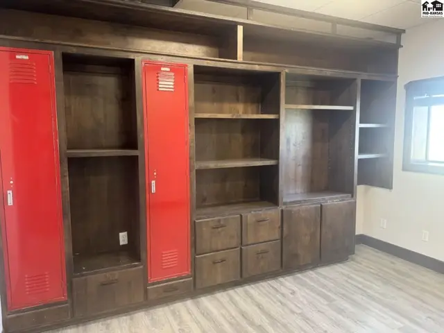 Built-in dark wood shelving unit with red locker doors and drawers, set against a light wood floor.