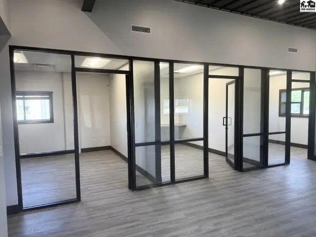 Modern office space with frosted glass partitions, black metal frames, and light wood-look flooring.