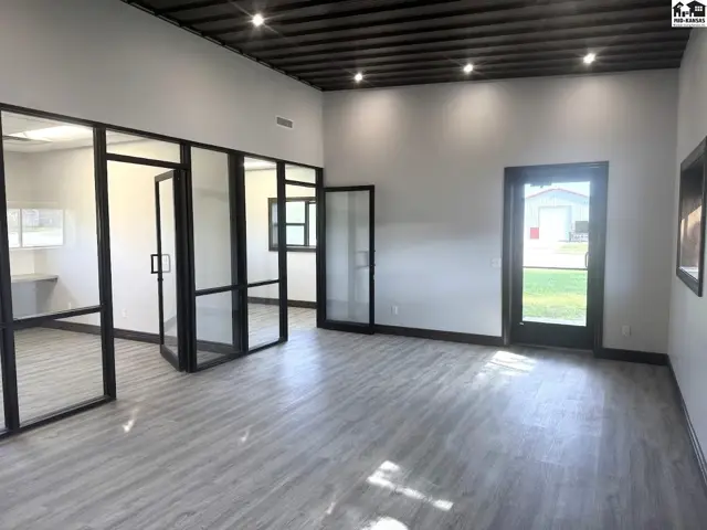 Modern office space with glass partitions, gray wood-look flooring, and dark metal ceiling.
