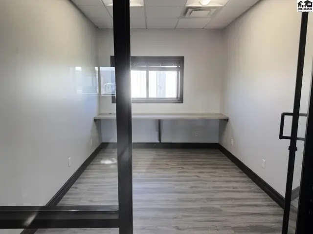 Empty office with light gray wood-look flooring, white walls, and built-in desk space.