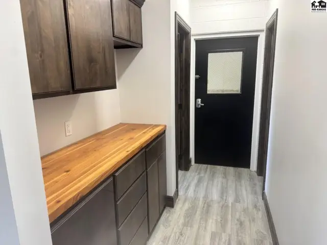 Hallway with dark wood cabinets, butcher block countertop, and a black door with a window.