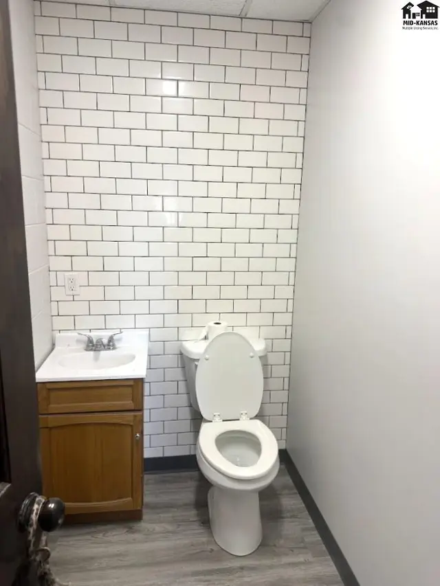 Modern bathroom with white subway tile, wood vanity, and gray wood-look flooring.