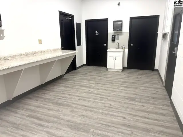 Modern restroom area with granite countertop, white vanity, and wood-look vinyl flooring.