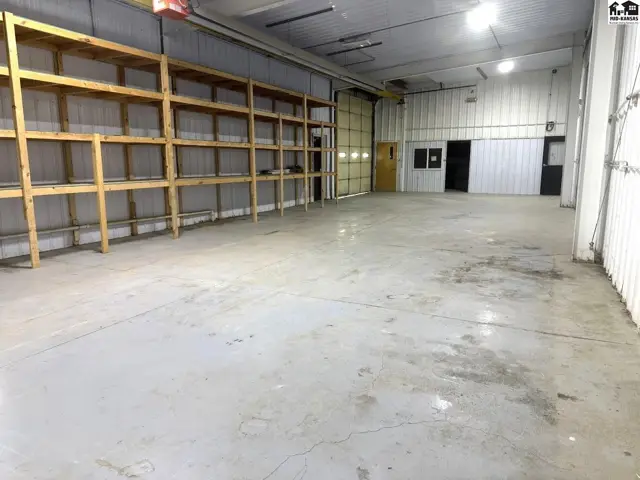 Spacious commercial interior with concrete floors, tall shelving, and a large roll-up door.