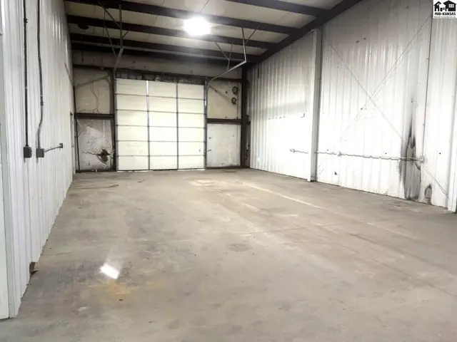 Spacious industrial interior with concrete floors, corrugated metal walls, and a large roll-up garage door.