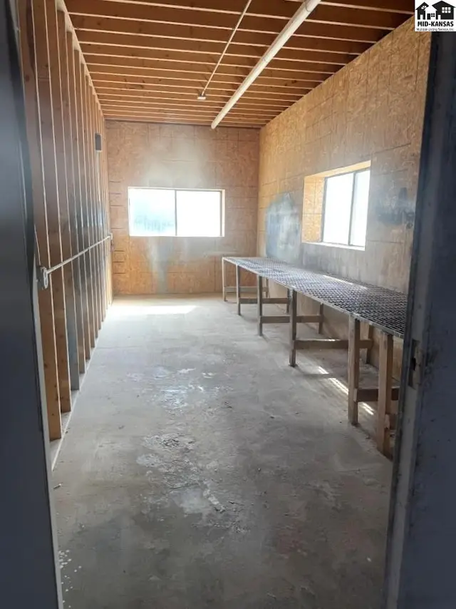 Empty room with unfinished wood walls, concrete floor, and two long wooden workbenches.
