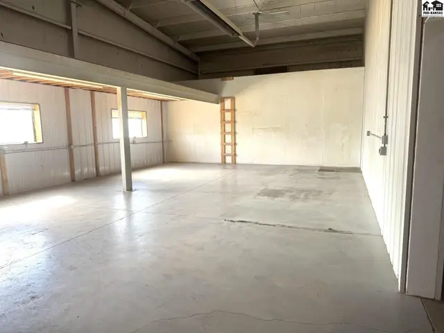 Spacious commercial interior with concrete floors, exposed beams, and white paneled walls.