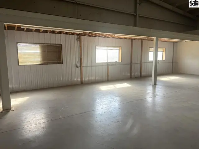 Spacious interior with concrete floors, corrugated metal walls, and large windows.