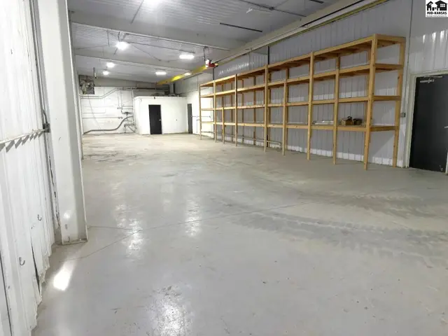 Spacious industrial space with concrete floors, metal walls, and extensive wooden shelving.