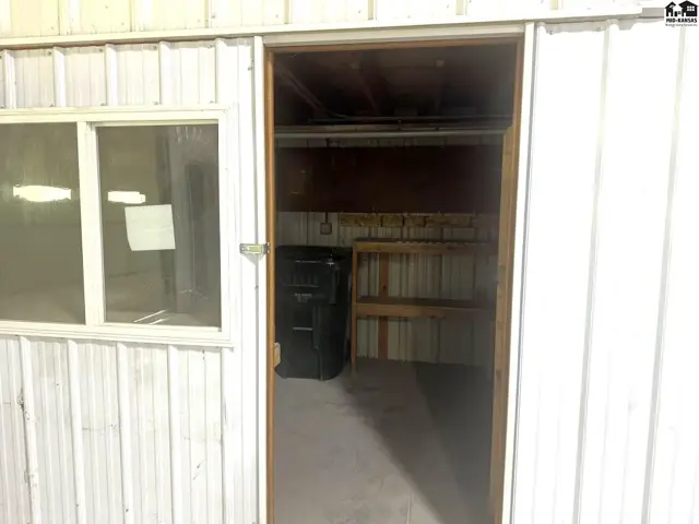 Interior view of a metal-sided room with a window, open doorway, and shelving.