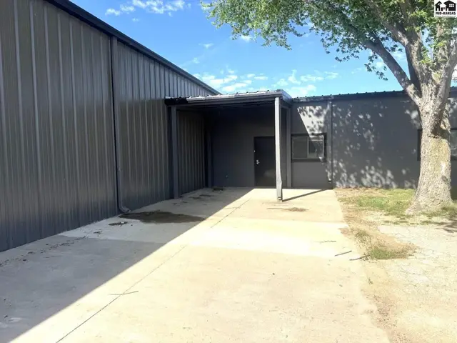 Exterior features a metal building with a covered entrance and a large tree.