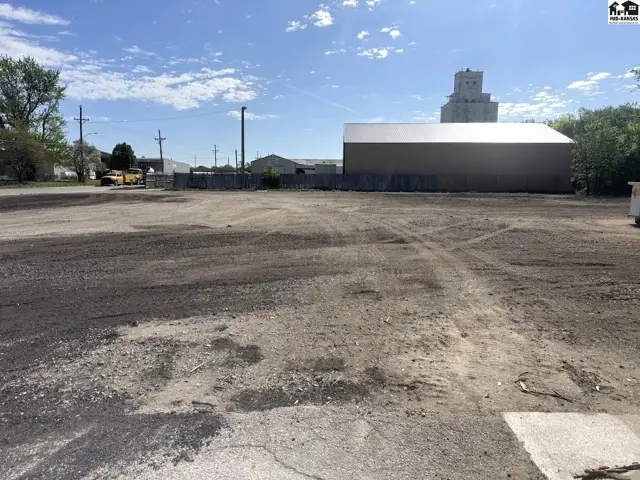 Expansive gravel lot with a large metal building and grain silo in the background.