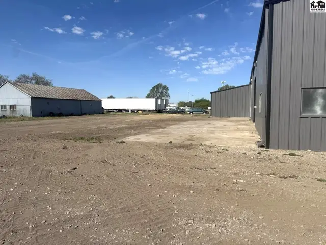 Exterior view of industrial buildings with metal siding and gravel lot under a blue sky.