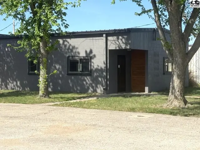 Modern gray stucco building with a wood-accented entrance and dark-framed windows.