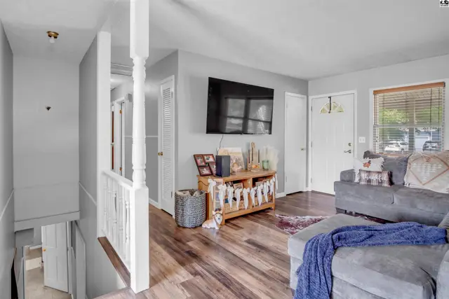 Spacious living room with gray sofa, wood-look flooring, and a mounted television above a wooden media console.