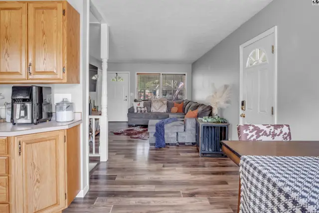 Spacious living room with gray walls, wood floors, and a sectional sofa, adjacent to a kitchen with oak cabinets.