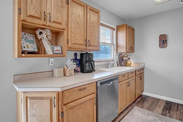 Bright kitchen with light oak cabinets, white countertops, stainless steel dishwasher, and wood-look flooring.