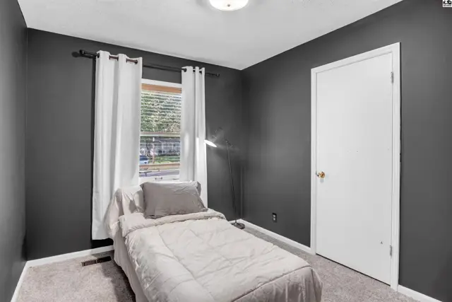Dark gray bedroom with a twin bed, white curtains, and a white door.