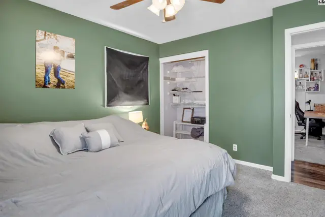 Green walls and gray carpet in a bedroom with an open closet and doorway to another room.