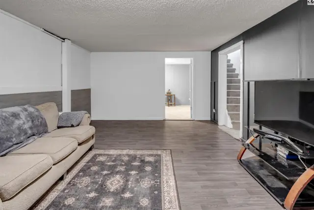 Spacious living area with a neutral sofa, dark wood-look flooring, and a gray accent wall.