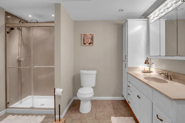 Modern bathroom with a glass-enclosed shower, white vanity, and beige tiled floor.