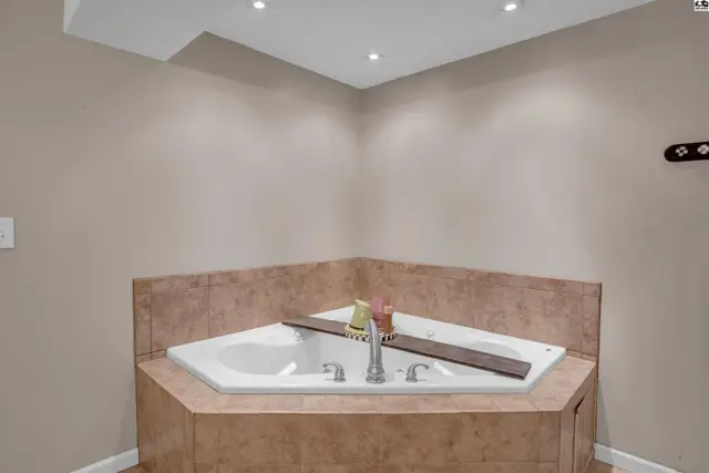 Corner jacuzzi tub with tiled surround and modern chrome fixtures in a neutral-toned bathroom.