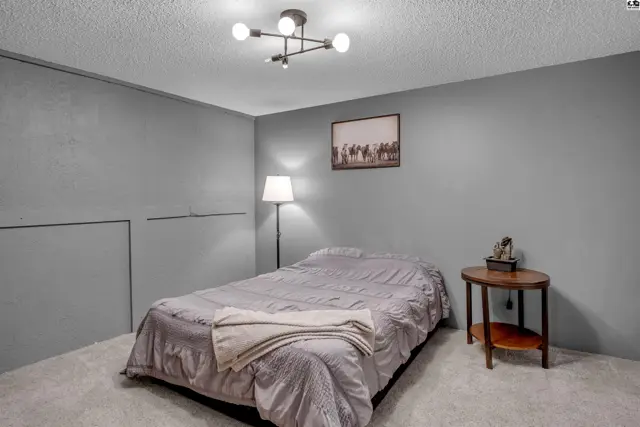 A bedroom with gray walls, a queen bed, and a modern light fixture.