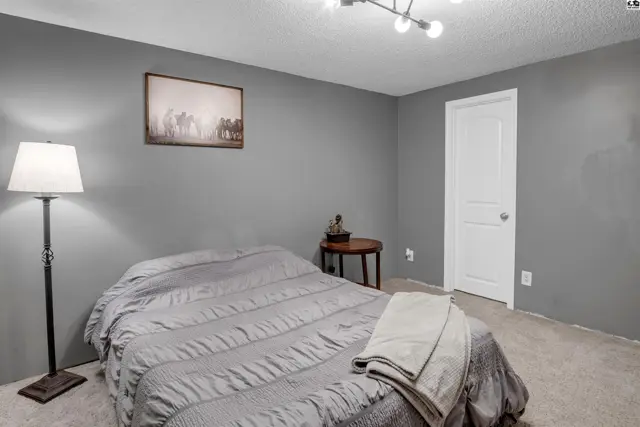 A bedroom with gray walls, a queen bed, and a modern light fixture.