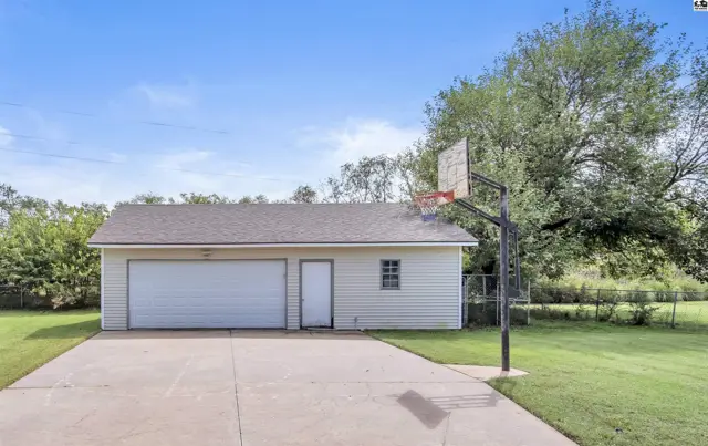 Two-car garage with a separate door, white siding, and a basketball hoop in the driveway.