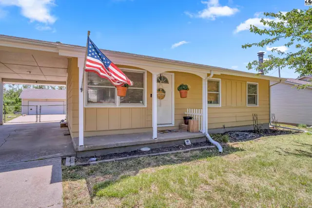 Yellow siding ranch home with a covered carport, white trim, and an American flag.