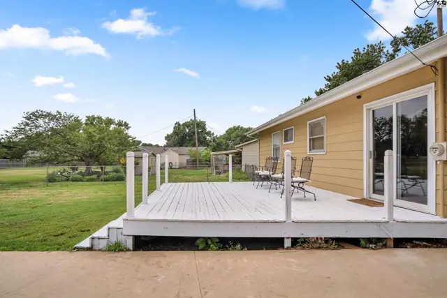 Spacious white deck with white railings and chairs overlooks a green backyard under a blue sky.