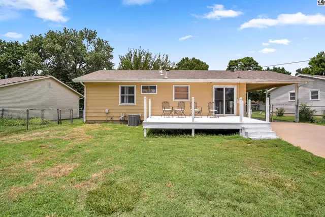 Yellow house exterior with a white deck, patio furniture, and attached carport.