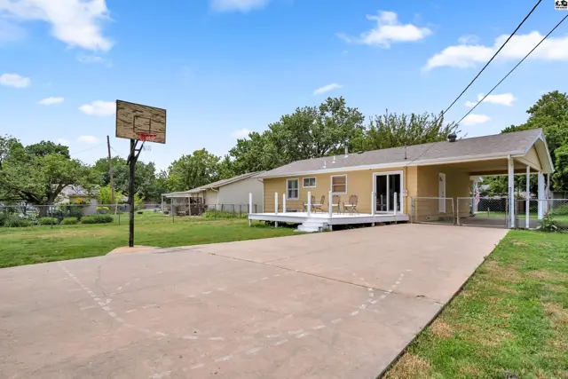Backyard features a basketball court, white deck, and covered carport attached to a yellow house.