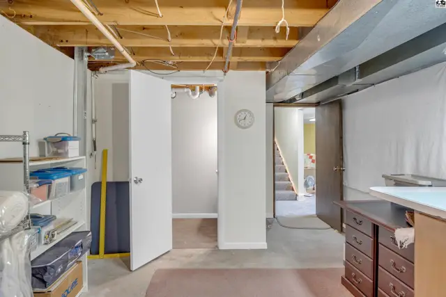 Unfinished basement with exposed joists, concrete floors, and a doorway leading to stairs.
